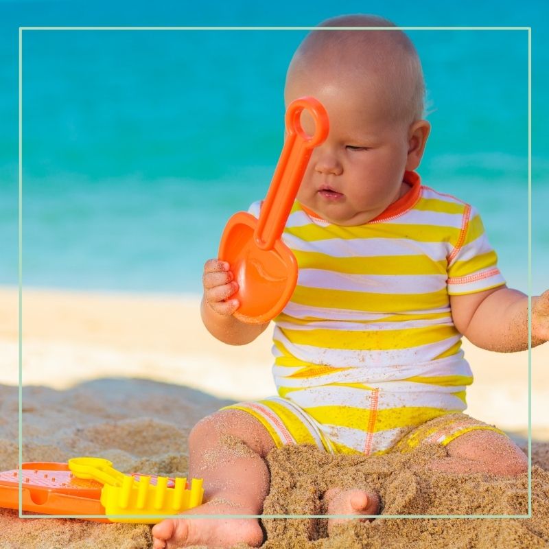 baby on beach playing with beach toys