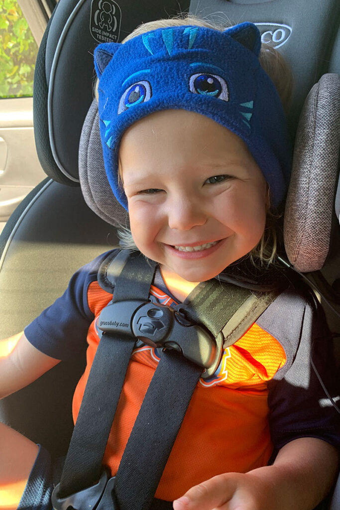 a happy child wearing a pair of CozyPhones Headband Toddler Headphones in a car seat.