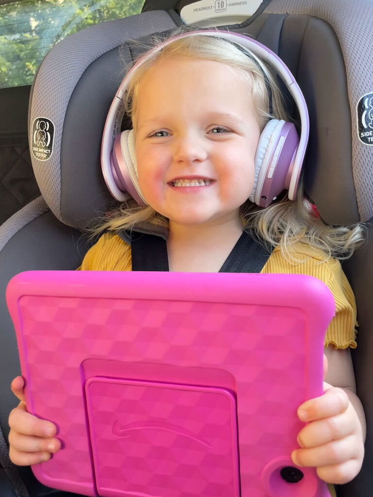 a happy child listens to PowerLocus Bluetooth Wireless headphones for toddlers in a car seat on a family road trip..