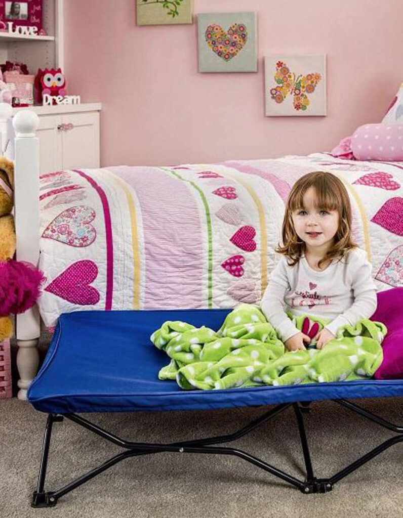 girl sitting on Regalo My Cot - foldable toddler bed for travel.