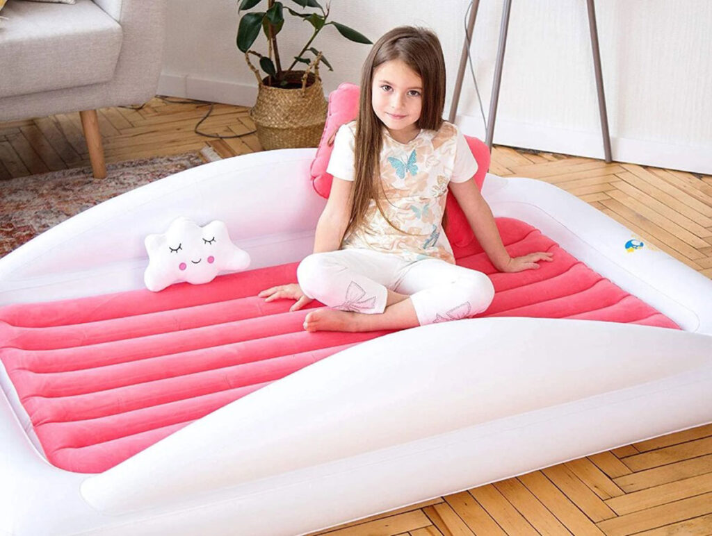 a young girl on a pink and white Sleepah inflatable toddler travel bed.