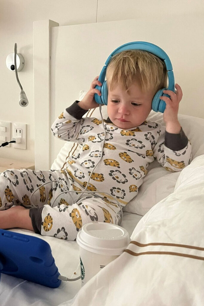 a child listens to Snug Play+ Kids Headphones for Toddlers in a hotel room on a family vacation.