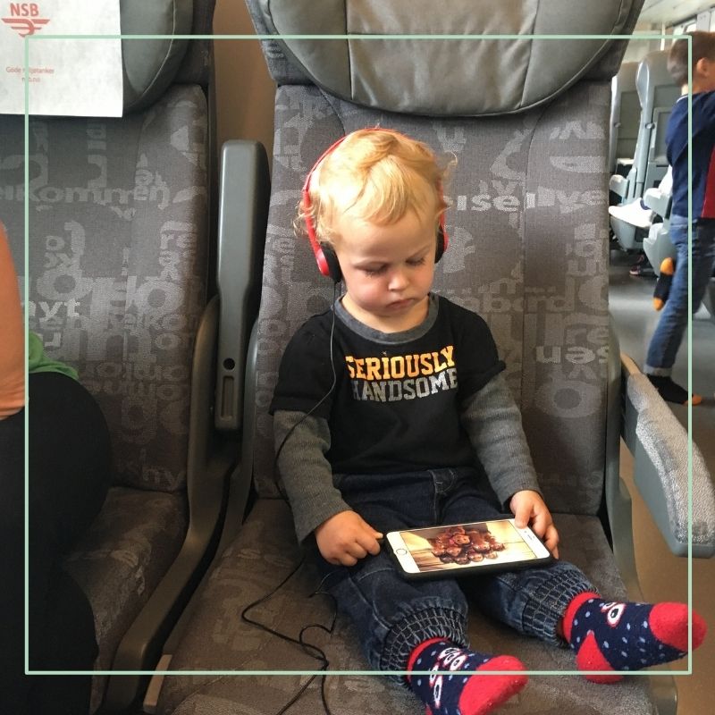 toddler on train with headphones and iphone