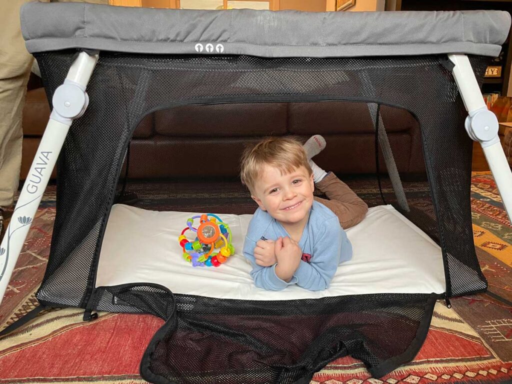 toddler in guava travel crib with side zipper door open