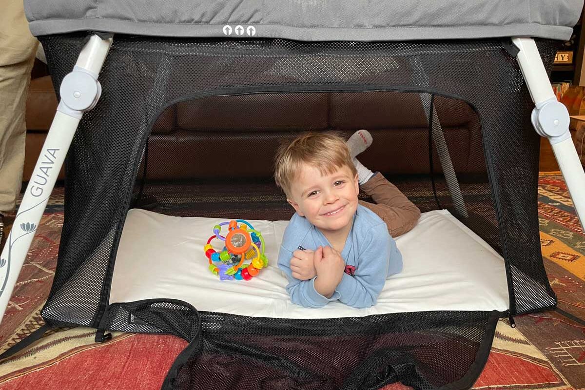 toddler in guava travel crib with side zipper door open