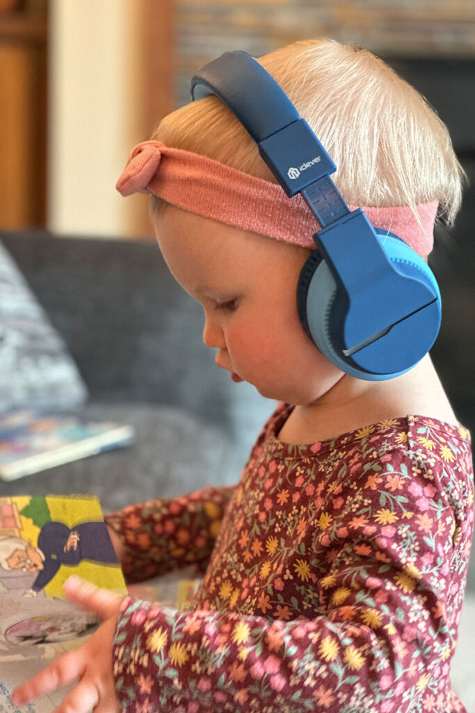 a small child reads a book while listening to music on iClever BTH12 toddler Bluetooth Headphones.