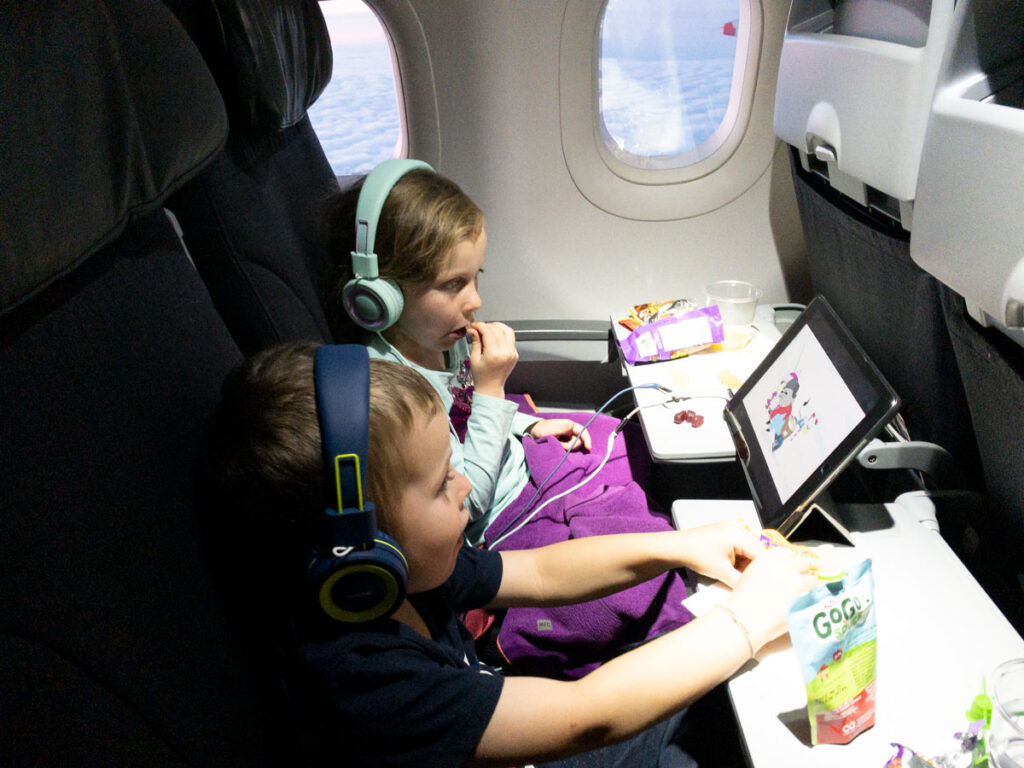 siblings watch the same iPad using the sharing port on their toddler headphones for planes.