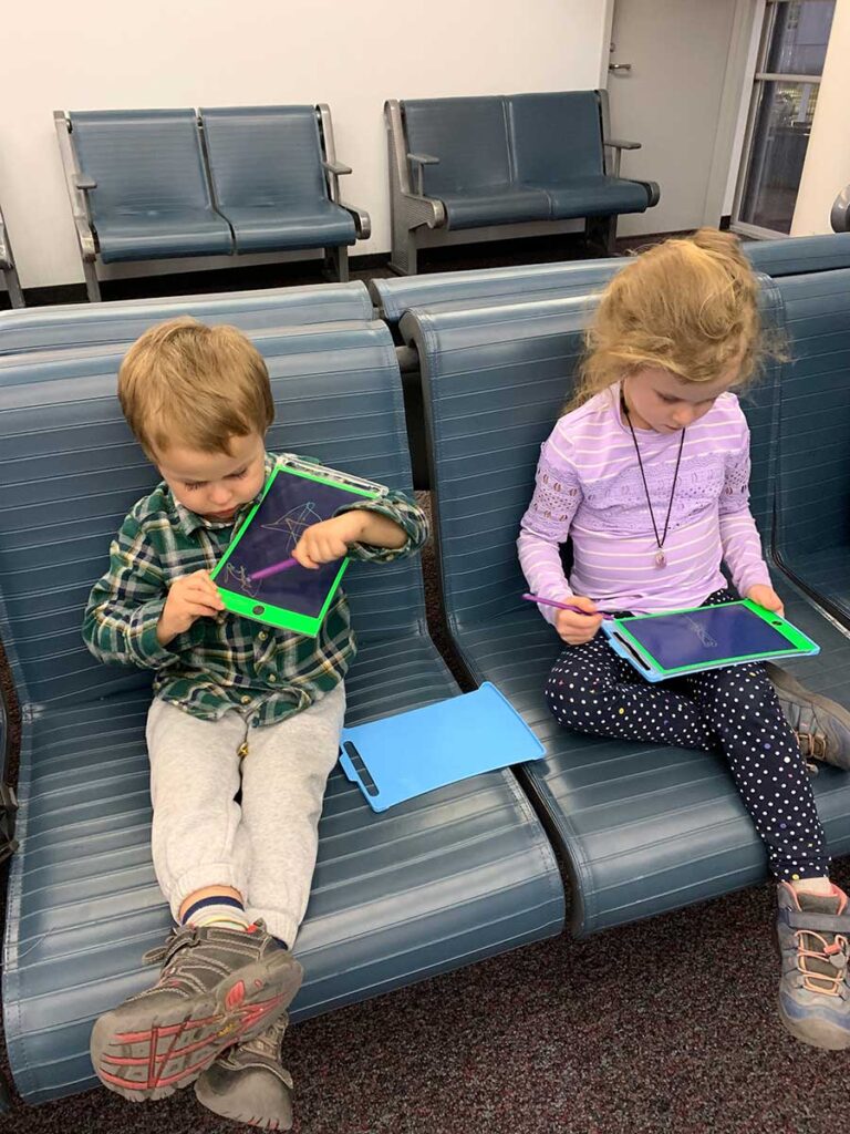 3 year old and older sister using LCD writing tablets while on a family trip.