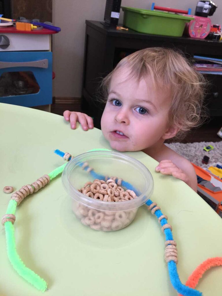 a BabyCanTravel.com toddler playing with DIY travel toy made from pipe cleaners and Cheerios.