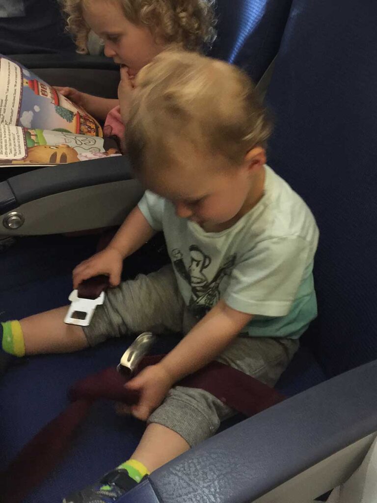 a toddler from the Baby Can Travel website  plays with a seatbelt on an airplane.