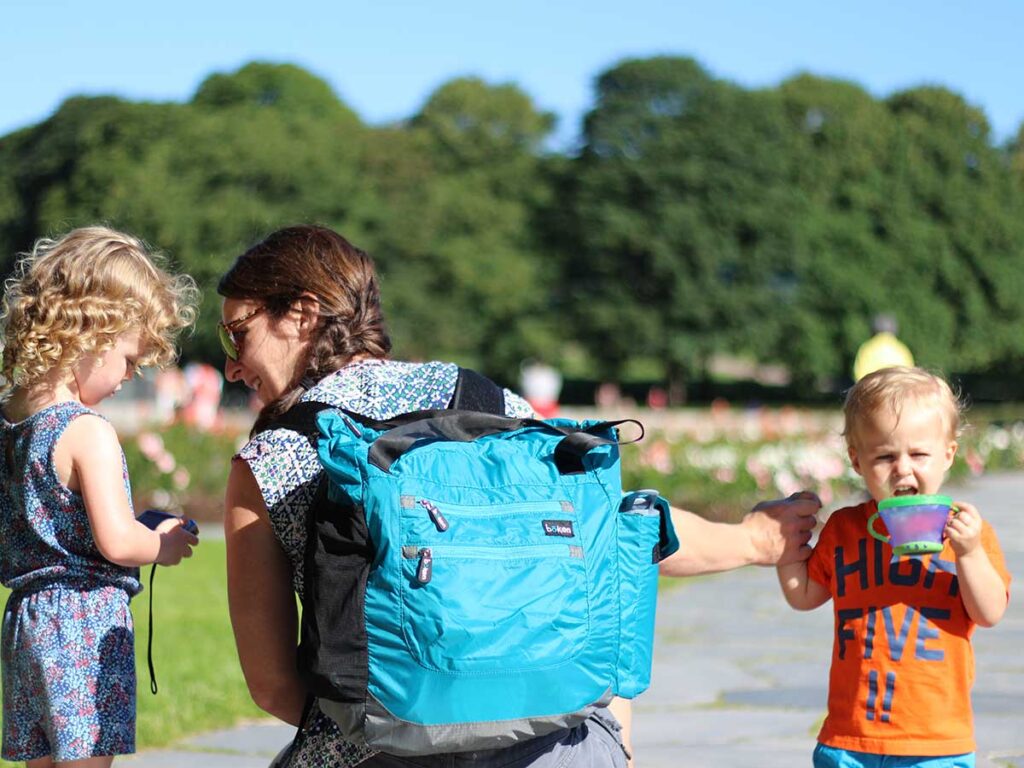 holding toddlers hand while wearing diaper bag backpack