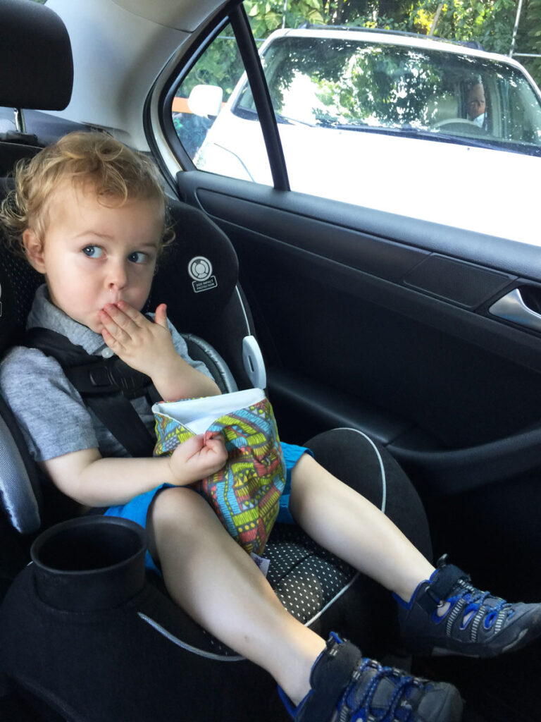 a toddler, from the BabyCanTravel.com family, eats a snack out of a reusable snack bag while on a family road trip.