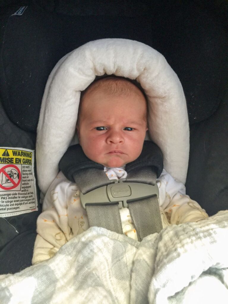 a baby boy sits in his car seat on a long car trip.