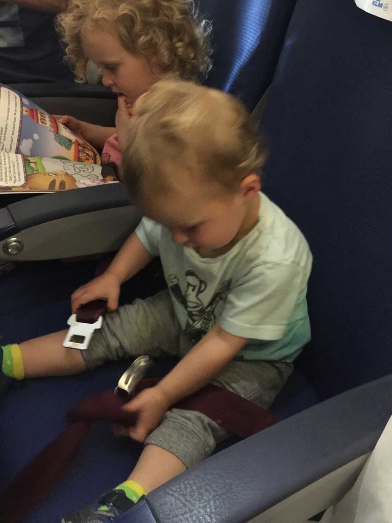 a BabyCanTravel.com toddler entertains himself with a seat buckle during a family flight.