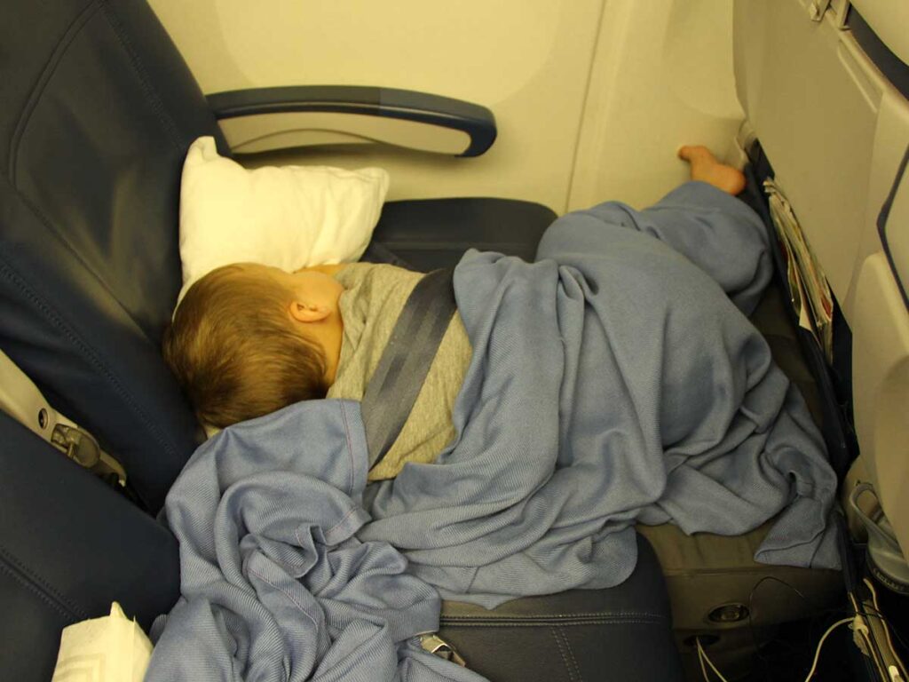 a BabyCanTravel.com toddler sleeps on an airplane using toddler airplane bed.