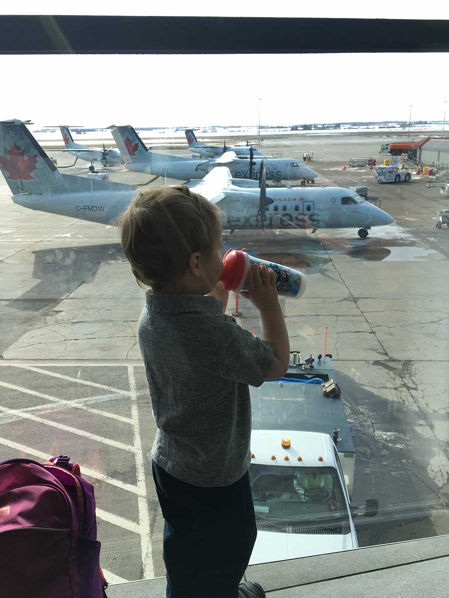 a toddler from the BabyCanTravel family, drinks out of his sippy cup at the airport before a family flight.