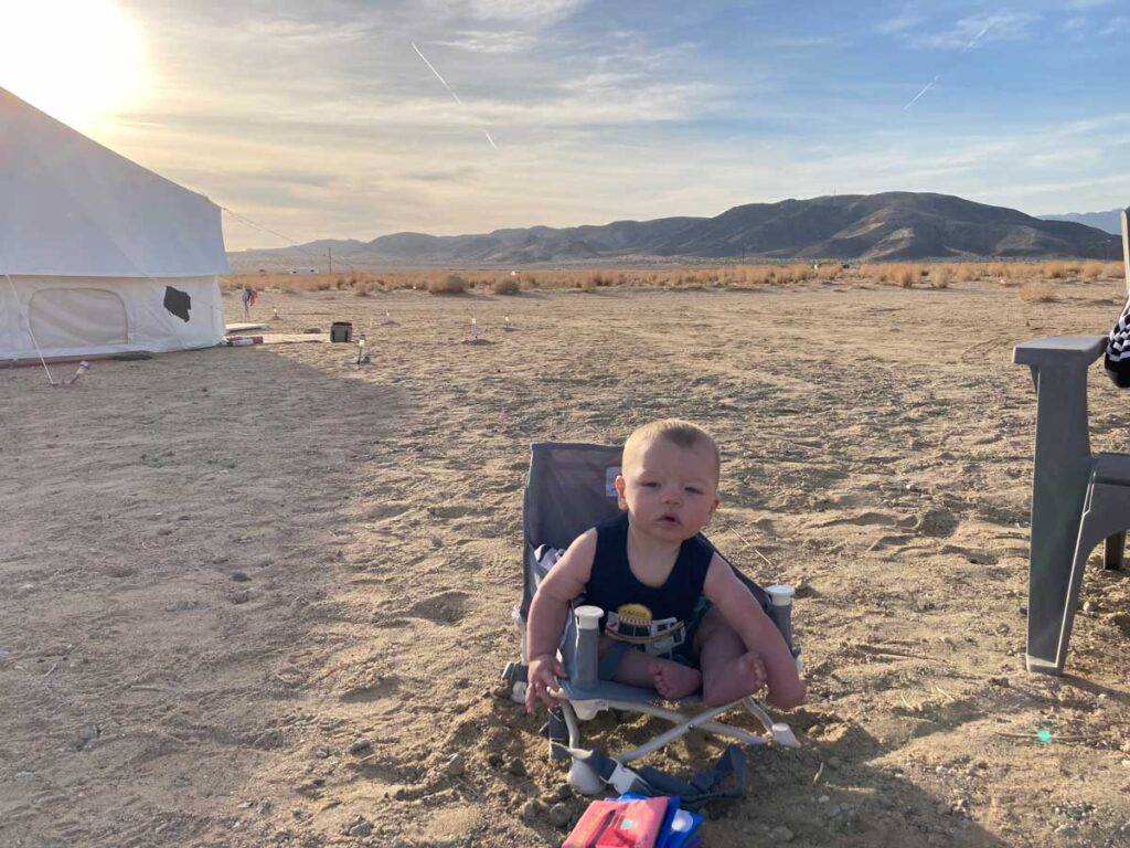 a baby sits in his hiccapop Booster Seat in the sand.