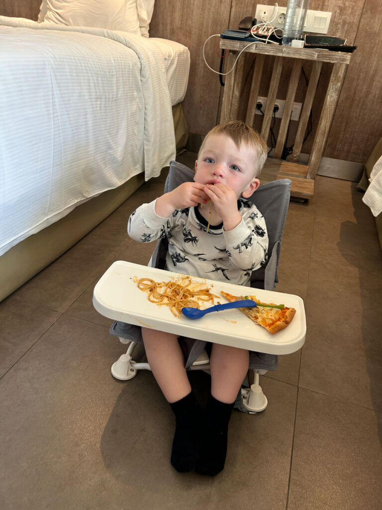 Baby sitting in booster seat in hotel room. 