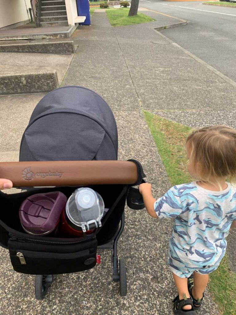 a toddler walks next to an ErgoBaby stroller.