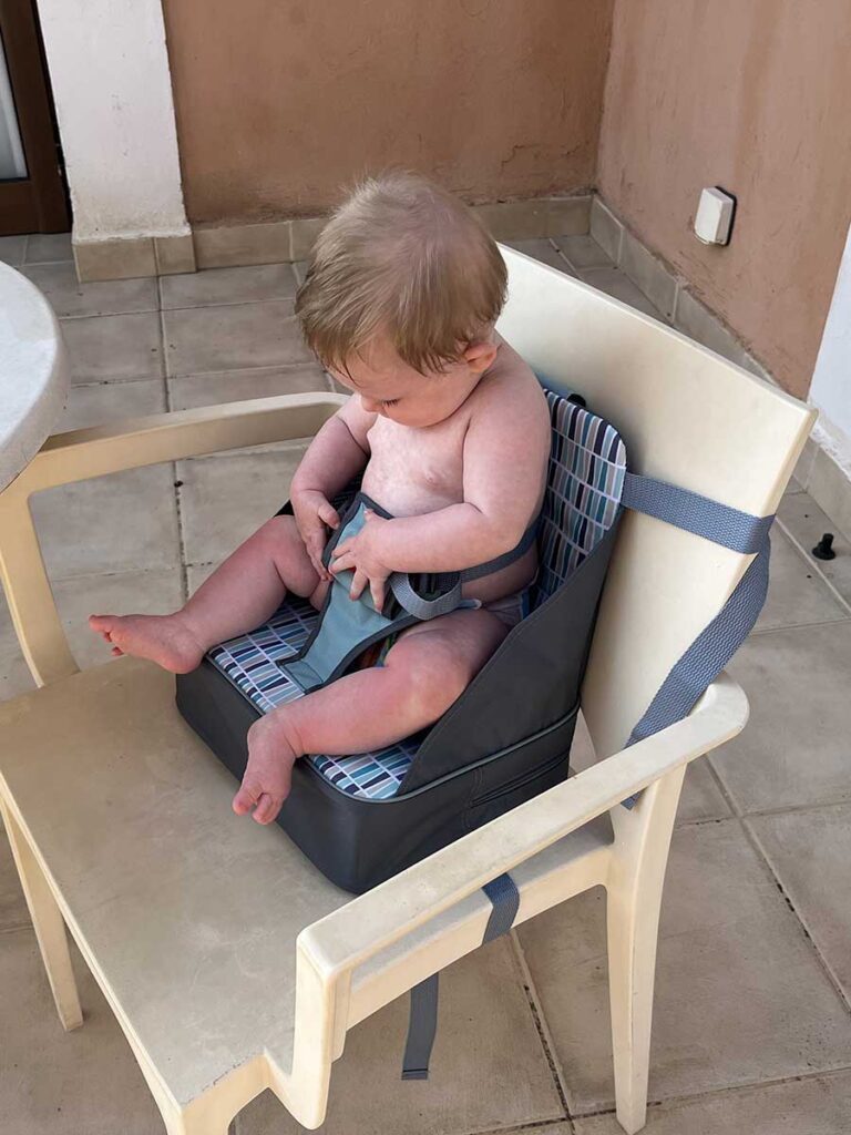 Baby in Nuby Travel highchair strapped to chair at table.