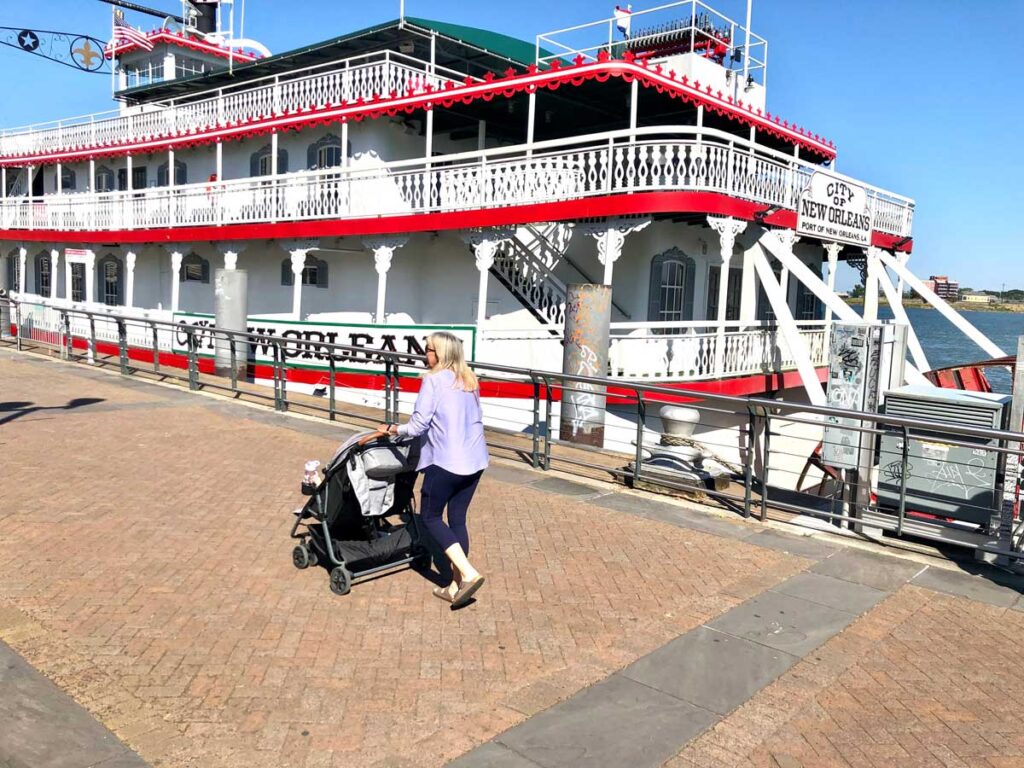 woman pushing stroller in front of riverboat.