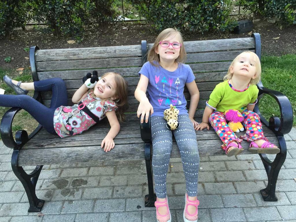 3 girls sitting on a park bench.