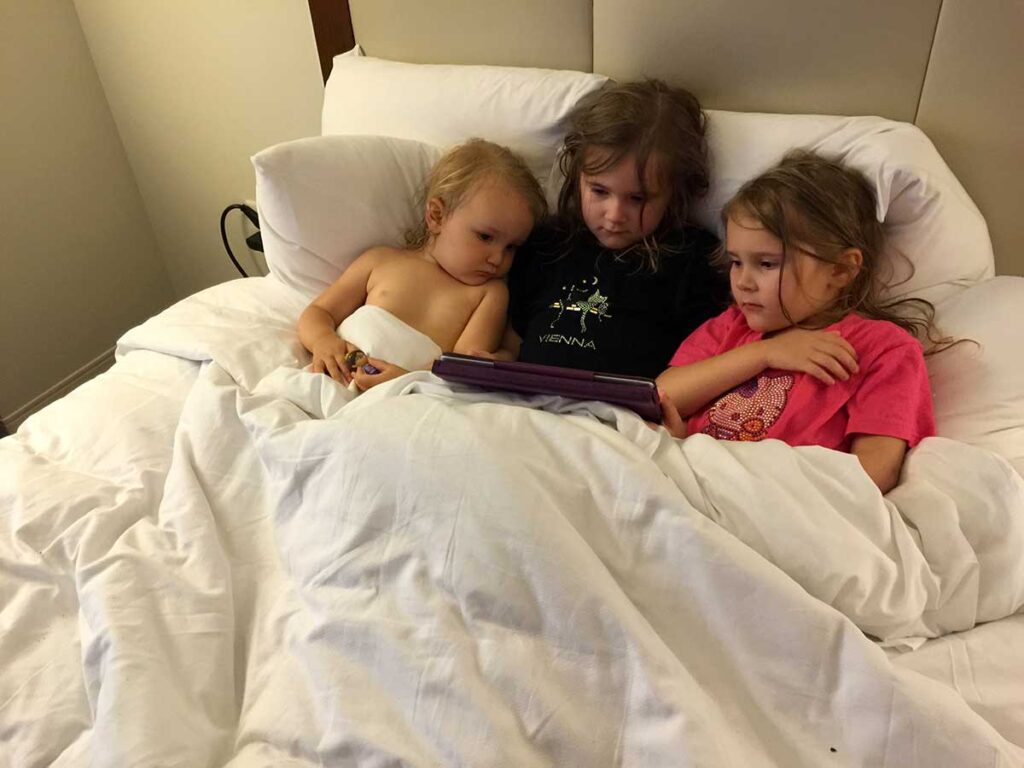 3 young girls in bed reading a book.