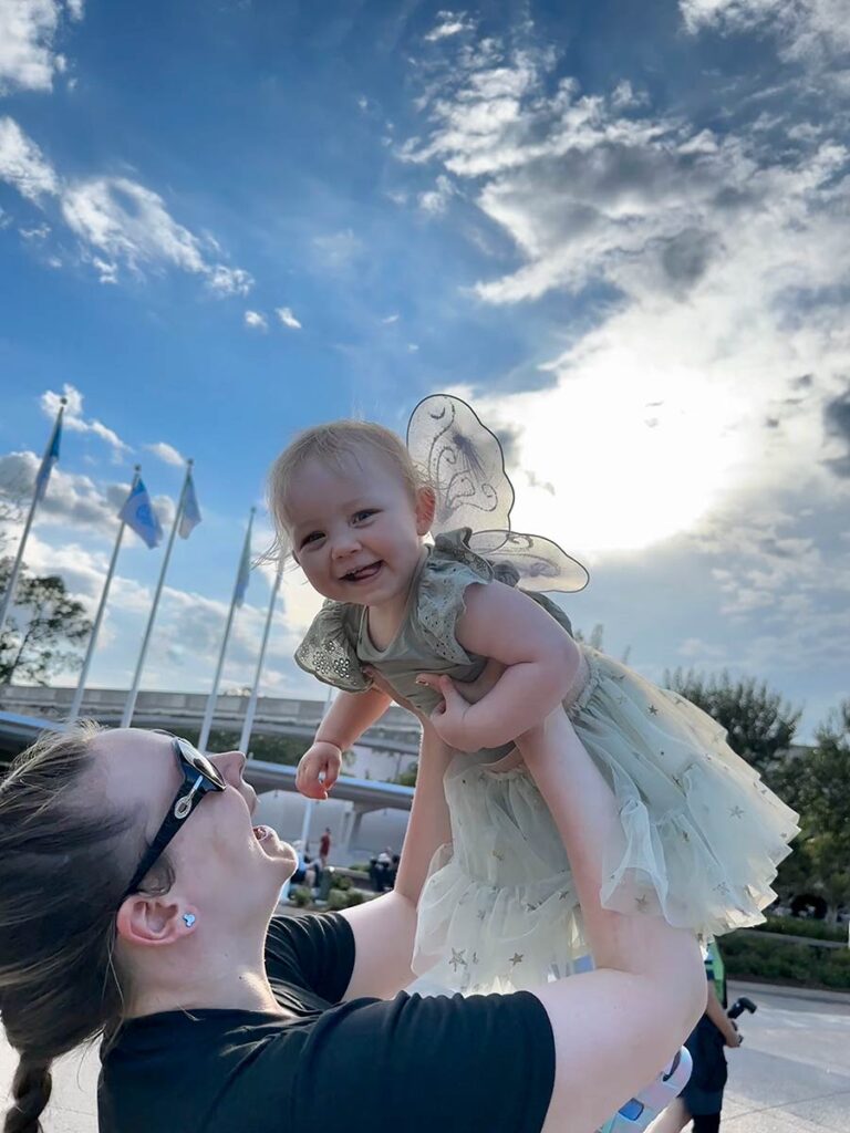 Mom holding up baby, who is dressed in a Disney character themed outfit.